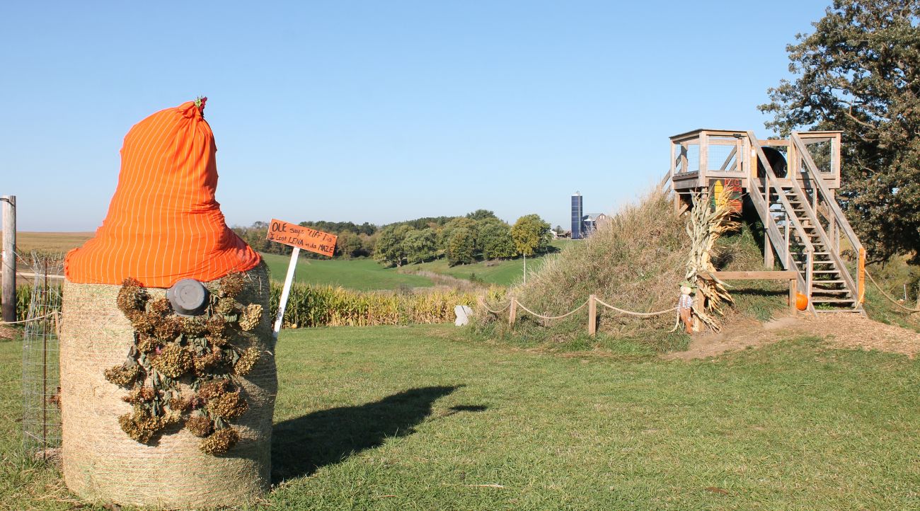 A haybale is transformed into a gnome with pinecone bear and orange hat.