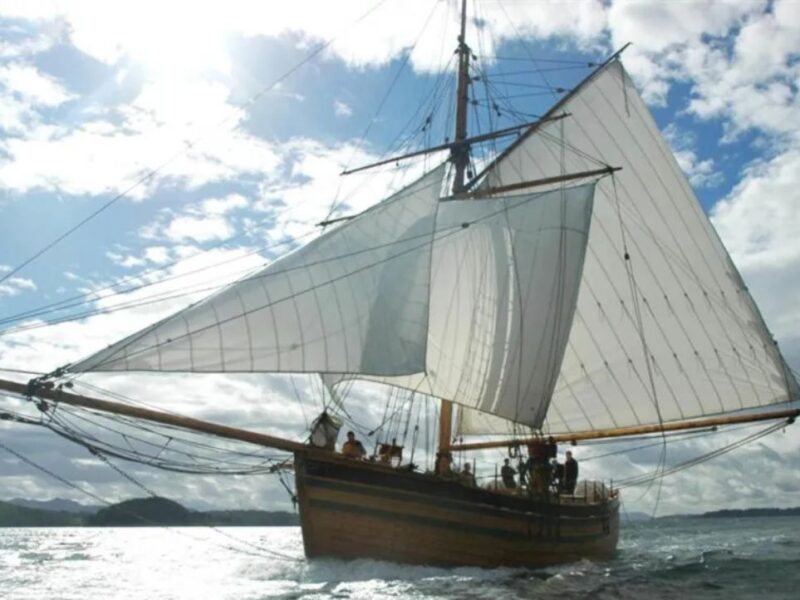 A replica of “The Restauration” Norwegian sailing ship shown at full sail on the sea with a bright blue sky with white clouds behind the sails.