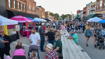 Small older main street with brightly colored tent set up as people gather, walk around, and visit with neighbors.