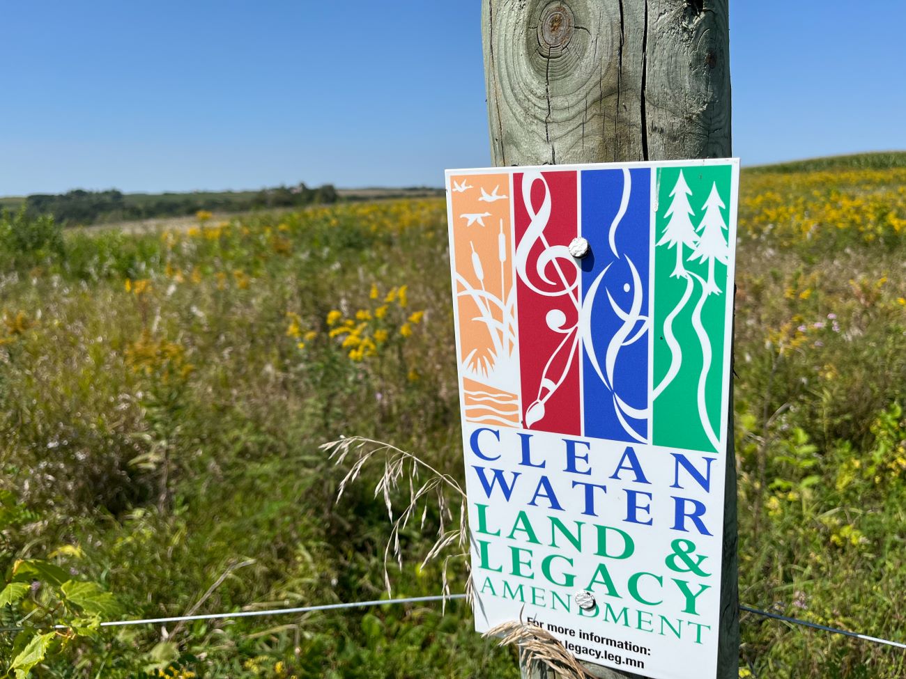 Brightly colored sign saying Clean Water Land and Legacy Amendment on a fence post in a prairie.