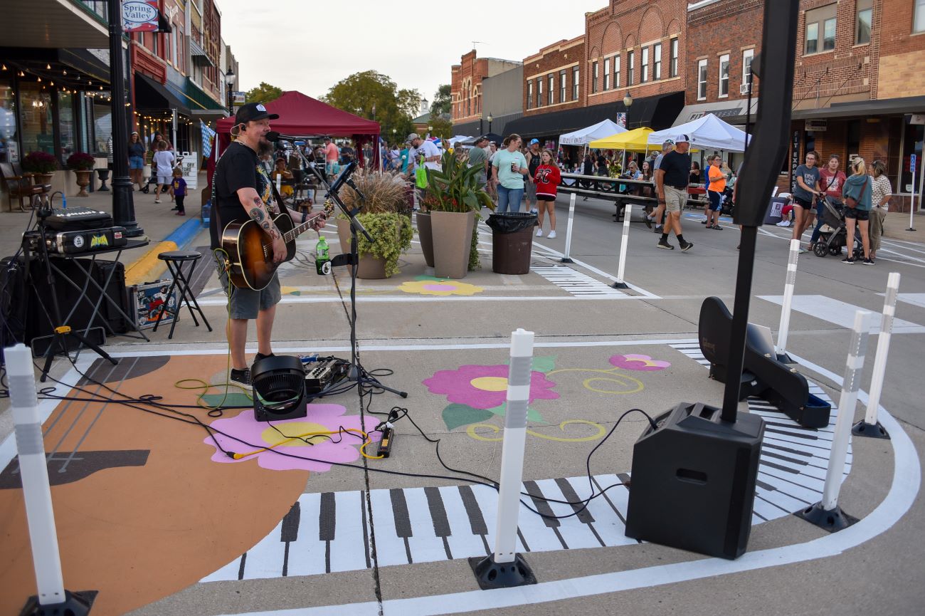 Musician plays on the sidewalk that is painted with a black and white piano keyboard that curves around a barrier.