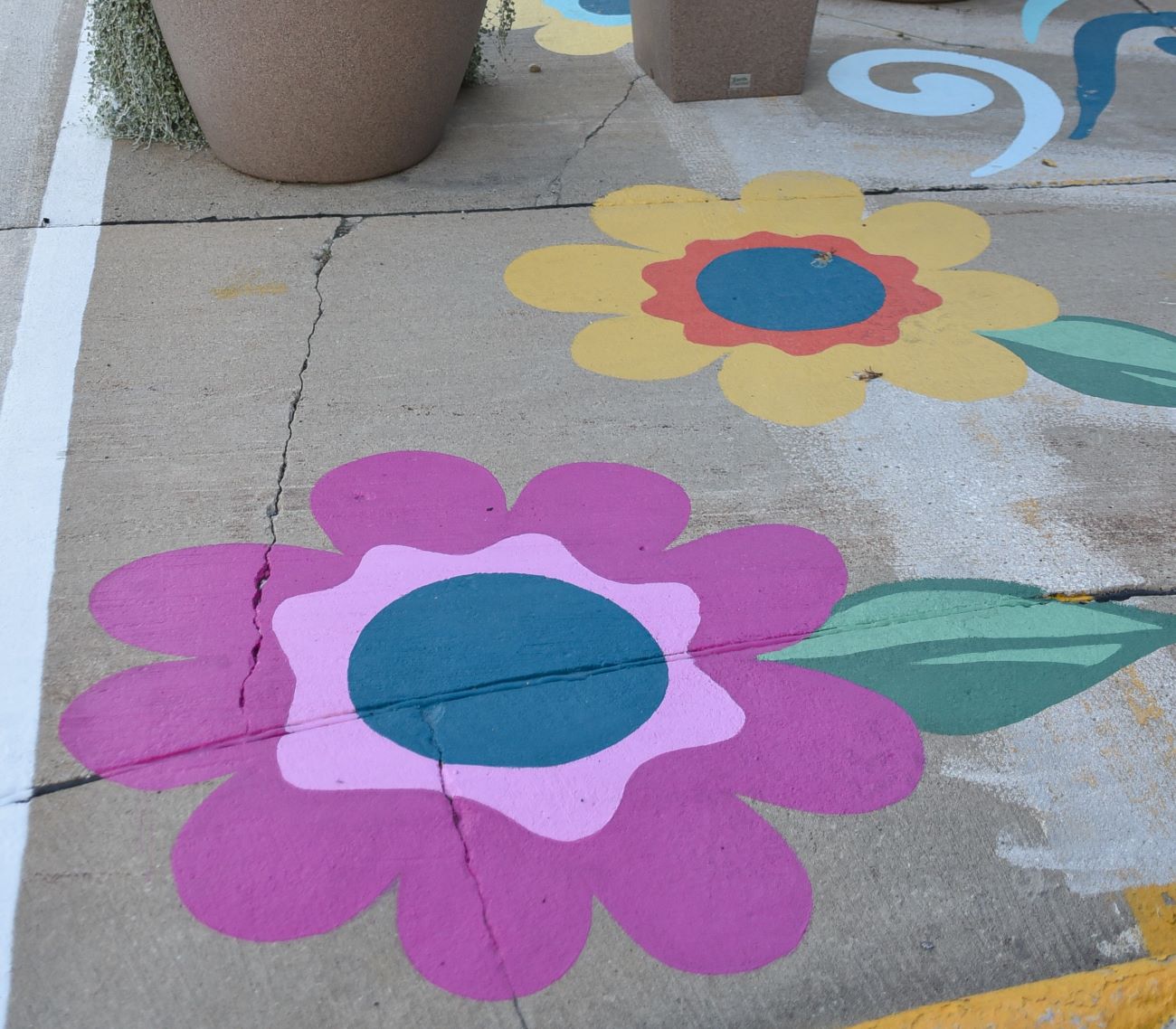 Pink flowers with blue centers and yellow flower with orange and blue center painted on the sidewalk.