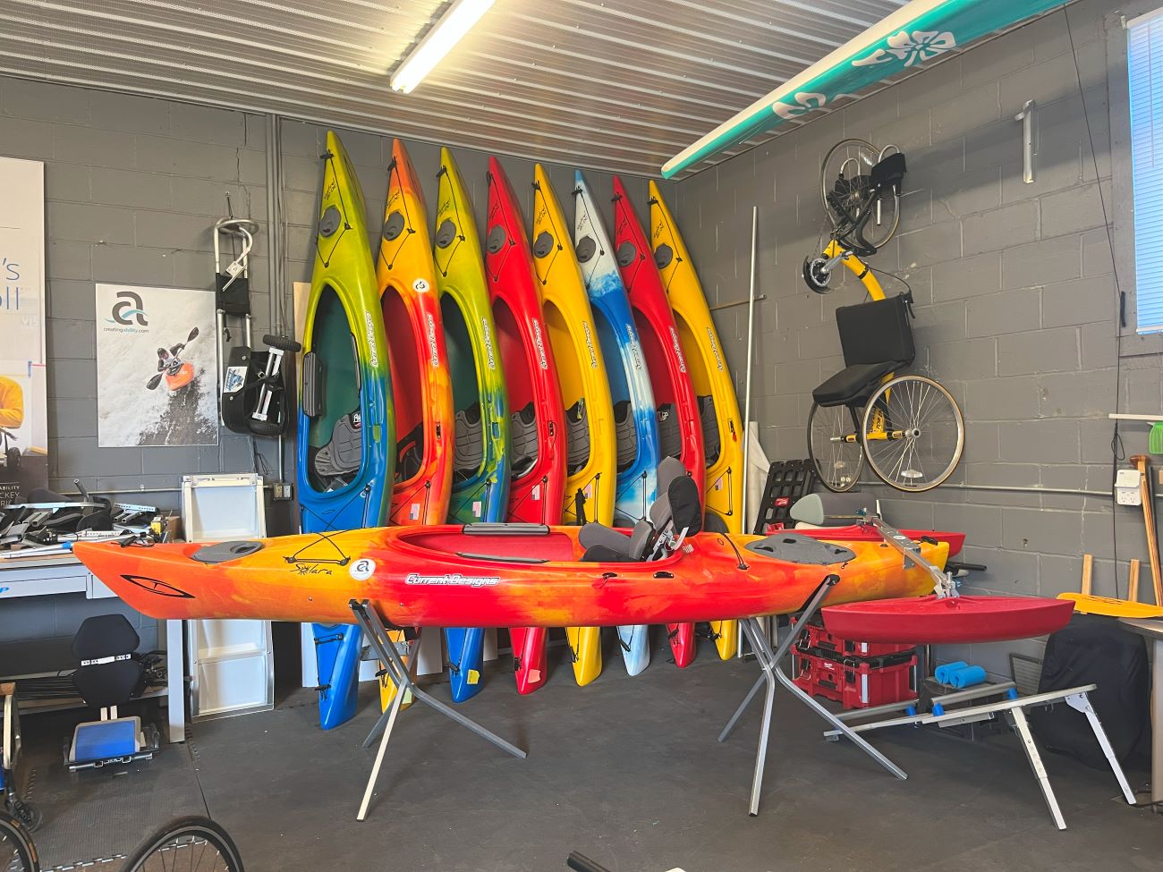 Blue, orange, red, and yellow kayaks lean upright with one setting in the foreground on braces.