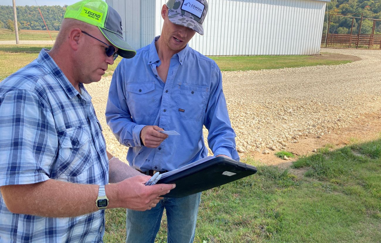 Two men dressed in farm work clothes look over plans for rotational grazing.