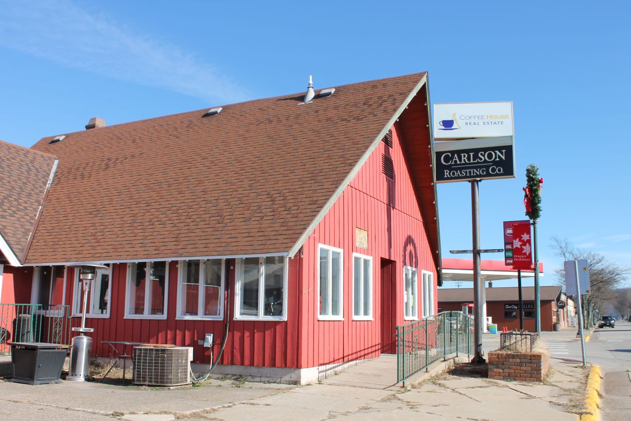 A bright read building with white trimmed windows and steeply pitched roof with a sign in the front.