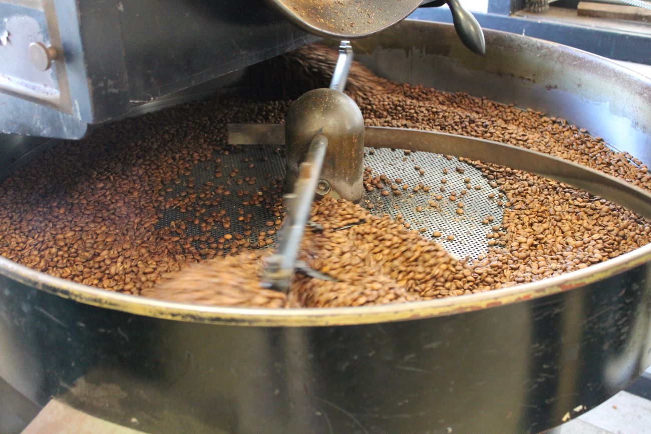 A long mechanical arm moves in a circular motion around a shallow tray holding coffee beans.