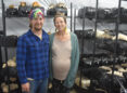 Couple stands in front of racks filled with growing mushrooms.