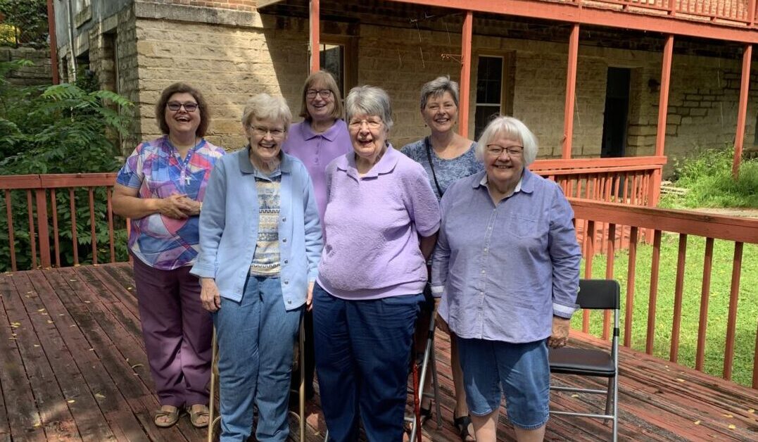 Group of women stand on a wooden deck.