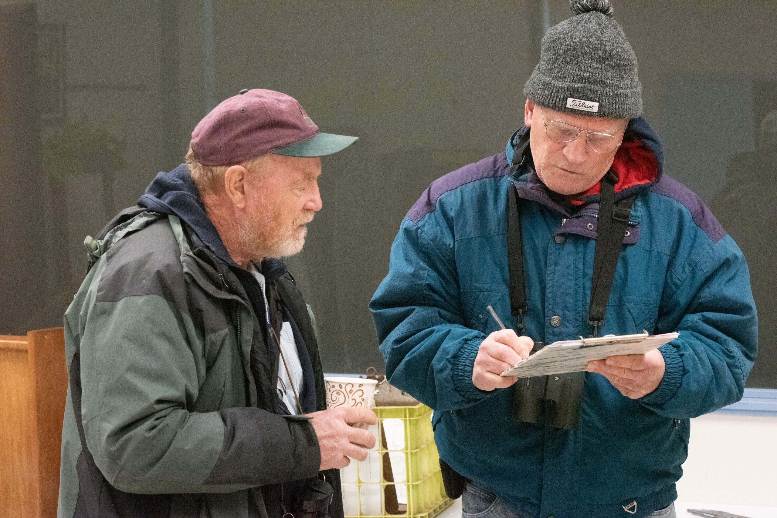 Two older men dressed in winter clothing look over a sheet on a clipboard after participating in the Christmas Bird Count at Whitewater State Park.