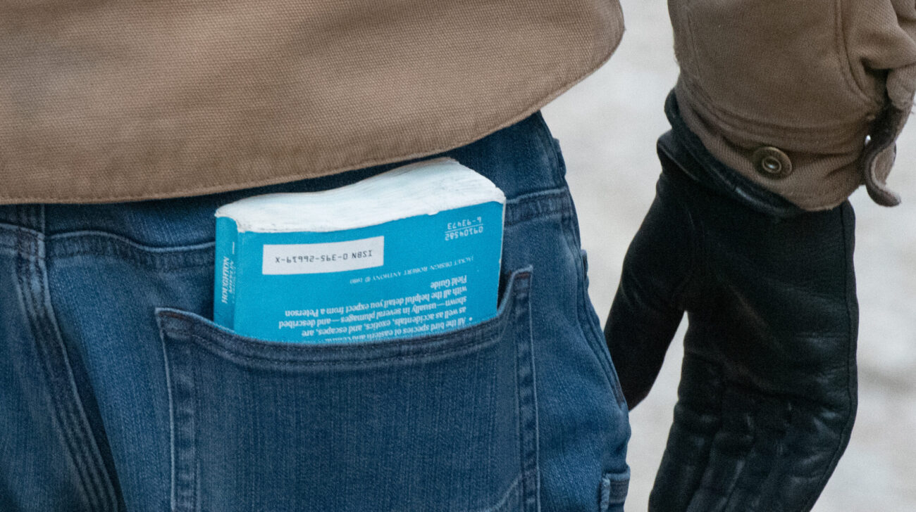 The bottom of light blue birding book peeks out of the back pocket of a man's denim jeans.