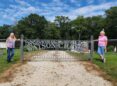 Two women stand in front of an iron gate with the words Watson Creek Cemetery