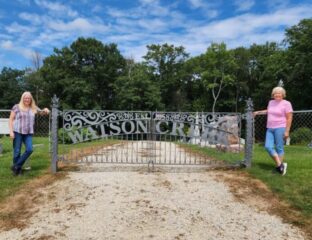 Two women stand in front of an iron gate with the words Watson Creek Cemetery