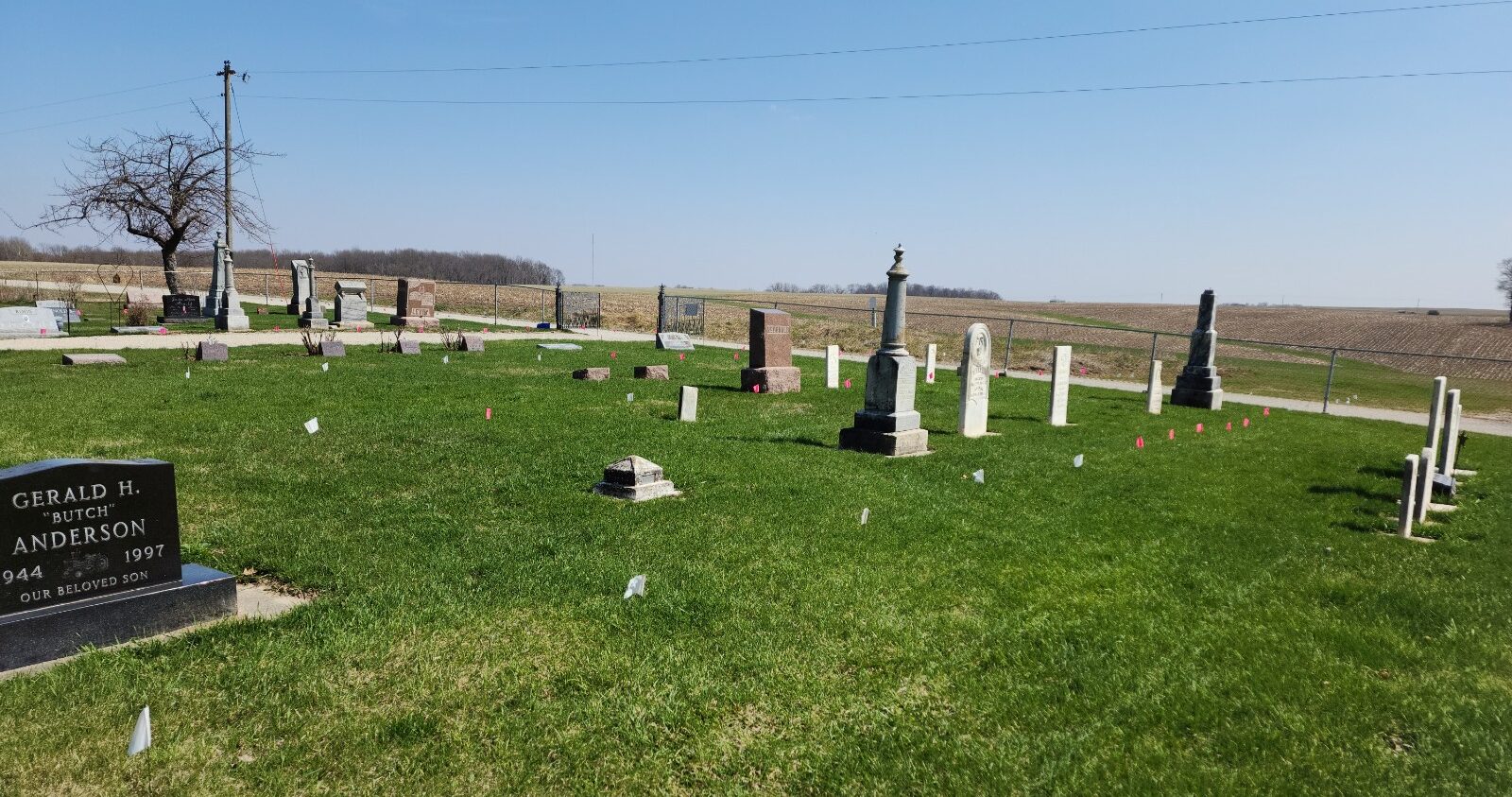 A green grassy field with blue sky is shown with headstones on the grass.