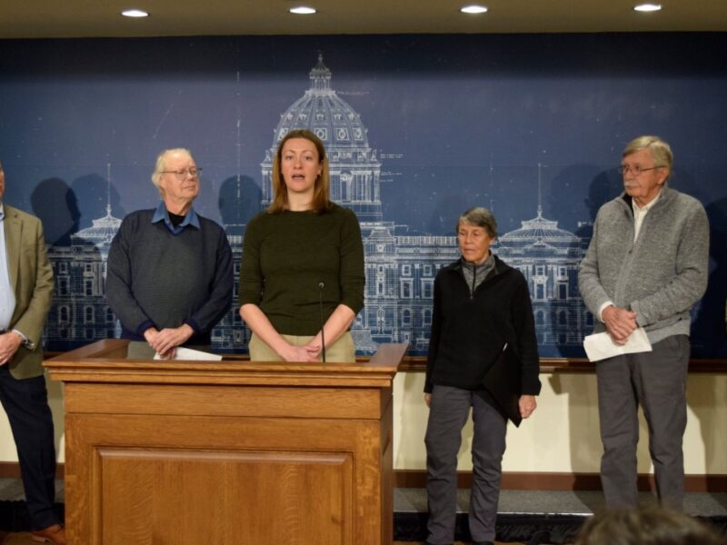 woman at podium with other adults surrounding her, announcing a minnesota law suit