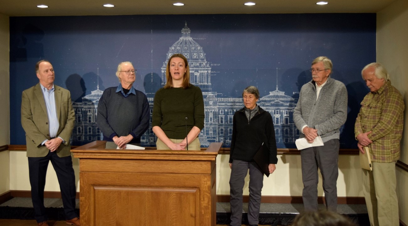 woman at podium with other adults surrounding her, announcing a minnesota law suit