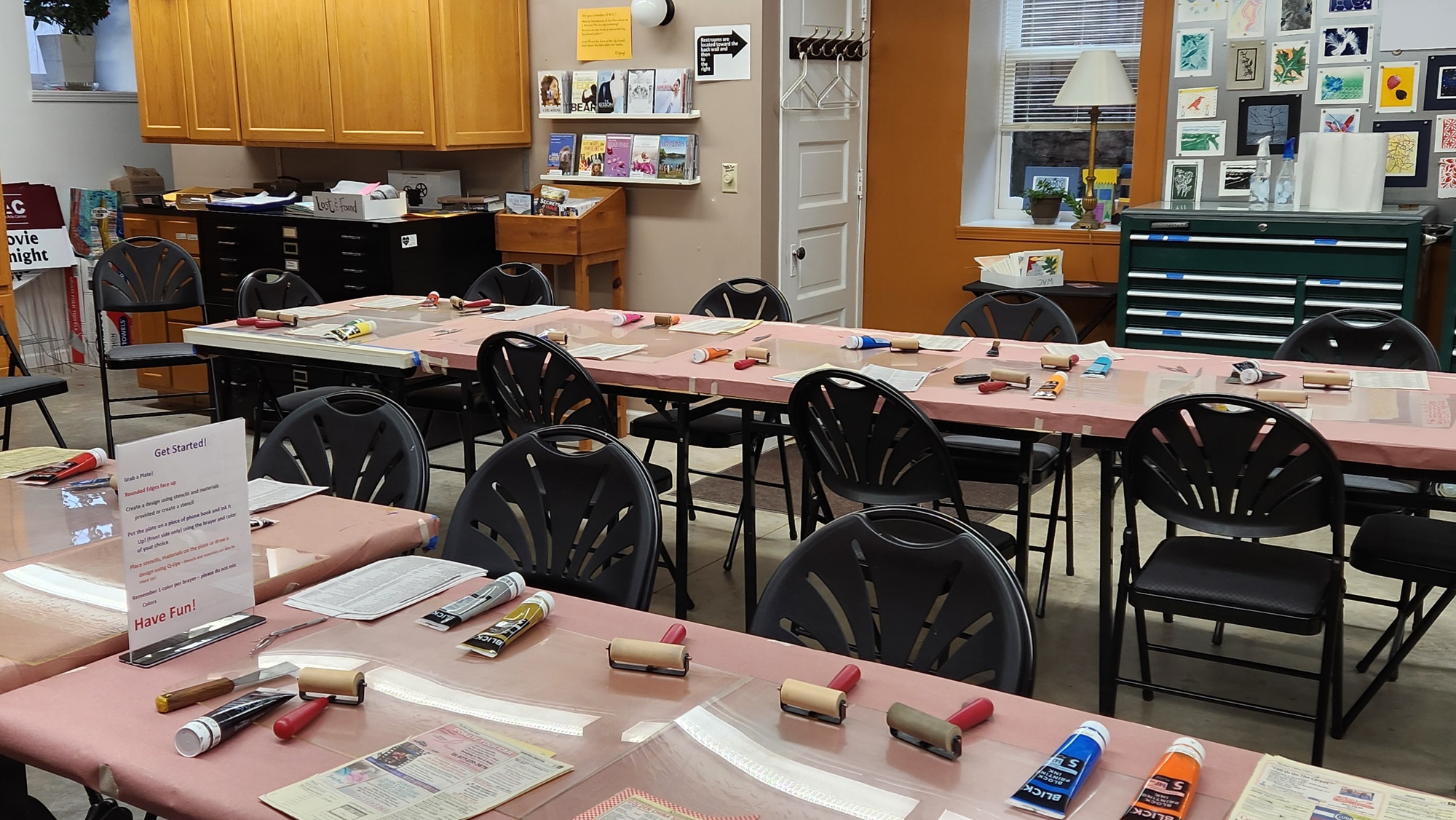 A classroom with long tables with paints, paper, and art tools laid out for students.