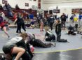 Girl wrestlers pair off as they warm up on the mat in a high school gym.