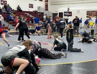 Girl wrestlers pair off as they warm up on the mat in a high school gym.