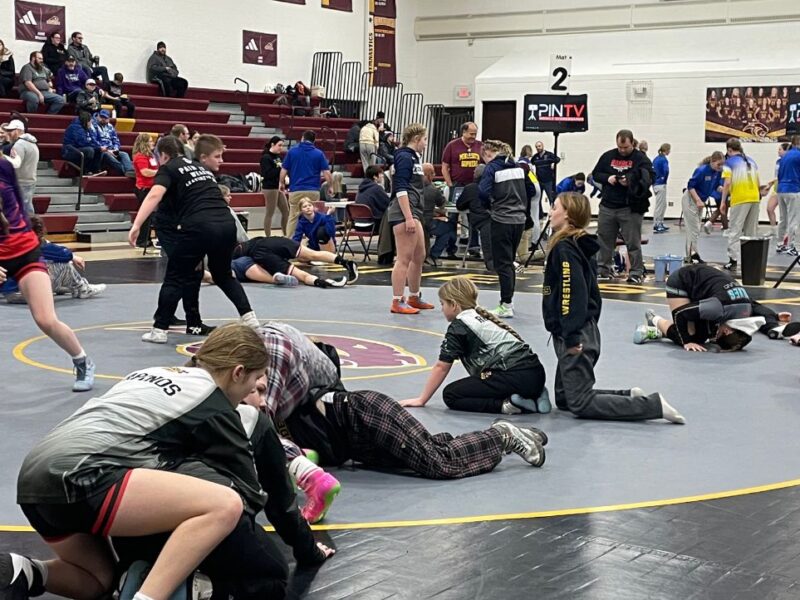 Girl wrestlers pair off as they warm up on the mat in a high school gym.