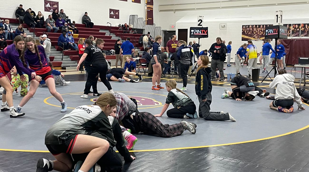 Girl wrestlers pair off as they warm up on the mat in a high school gym.