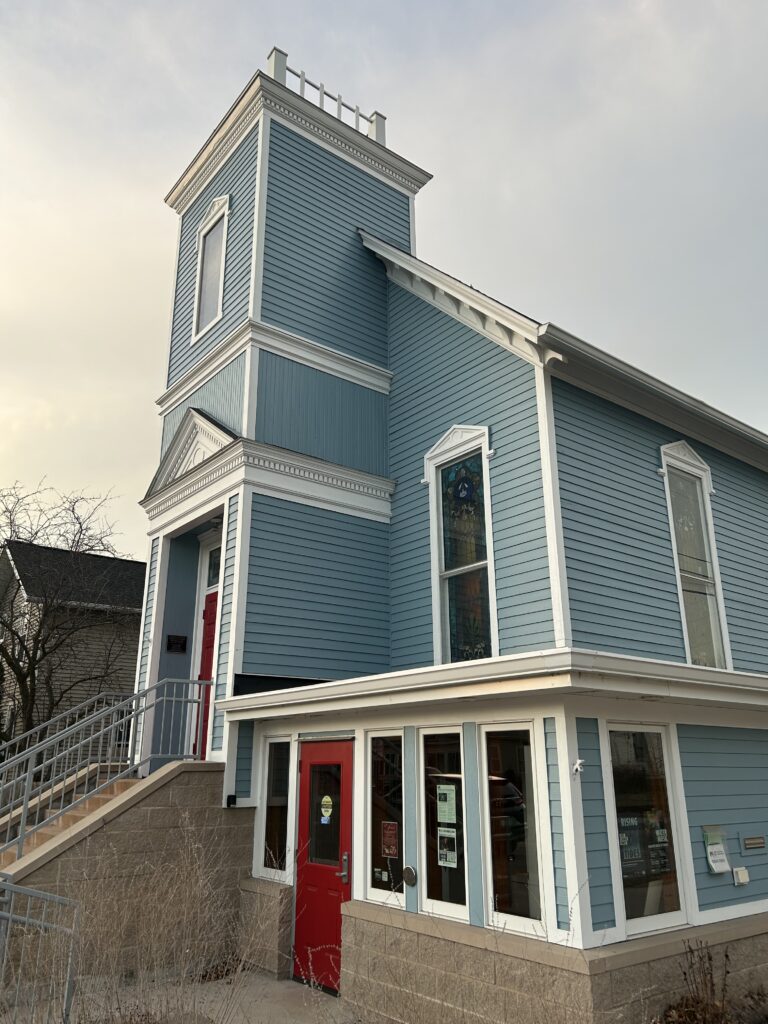 A light blue building with white trim and red door.