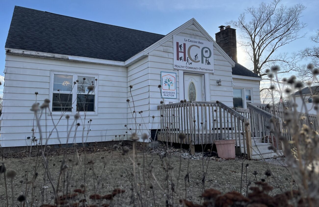 A small white house with a wooden front step and small stoop with a sign over the door saying HCP and Health Community Partnership