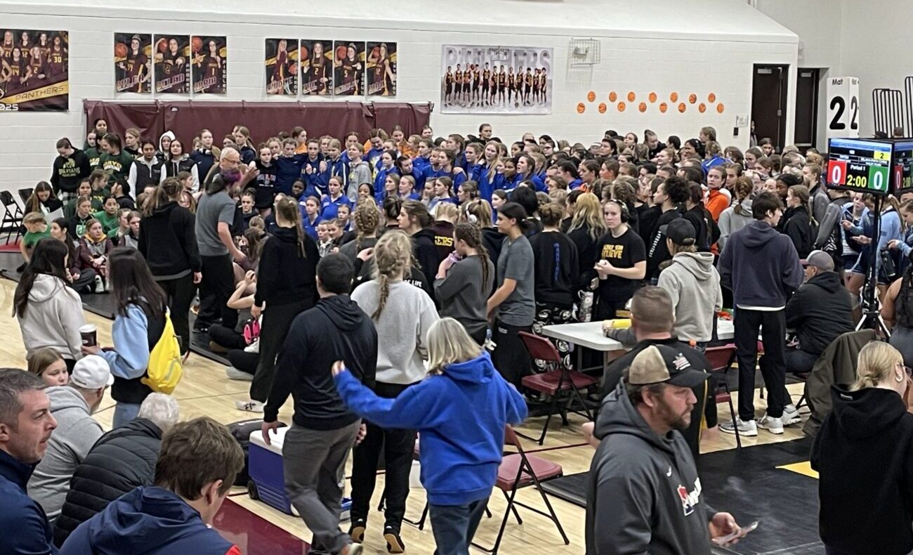 A large group of fans watch from high school bleachers as wrestling teams meet before the match.