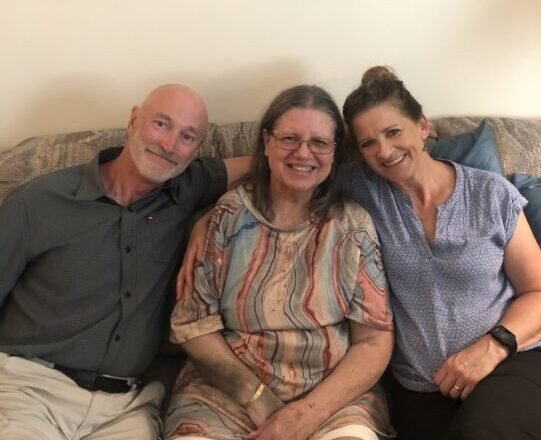 Three people lean into together while sitting on a couch.