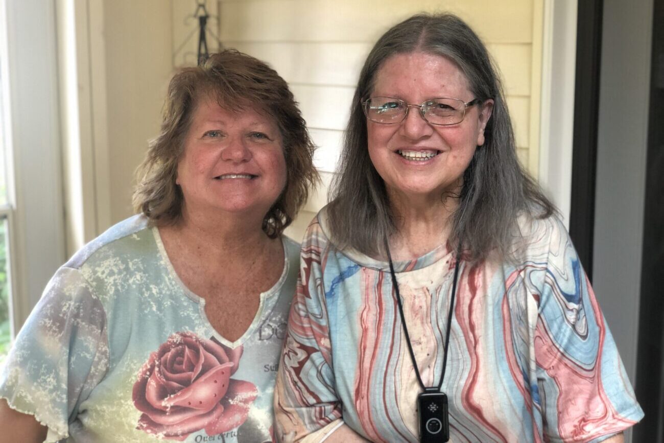 Two women both dressed in colorful, casual clothing smile at the camera.