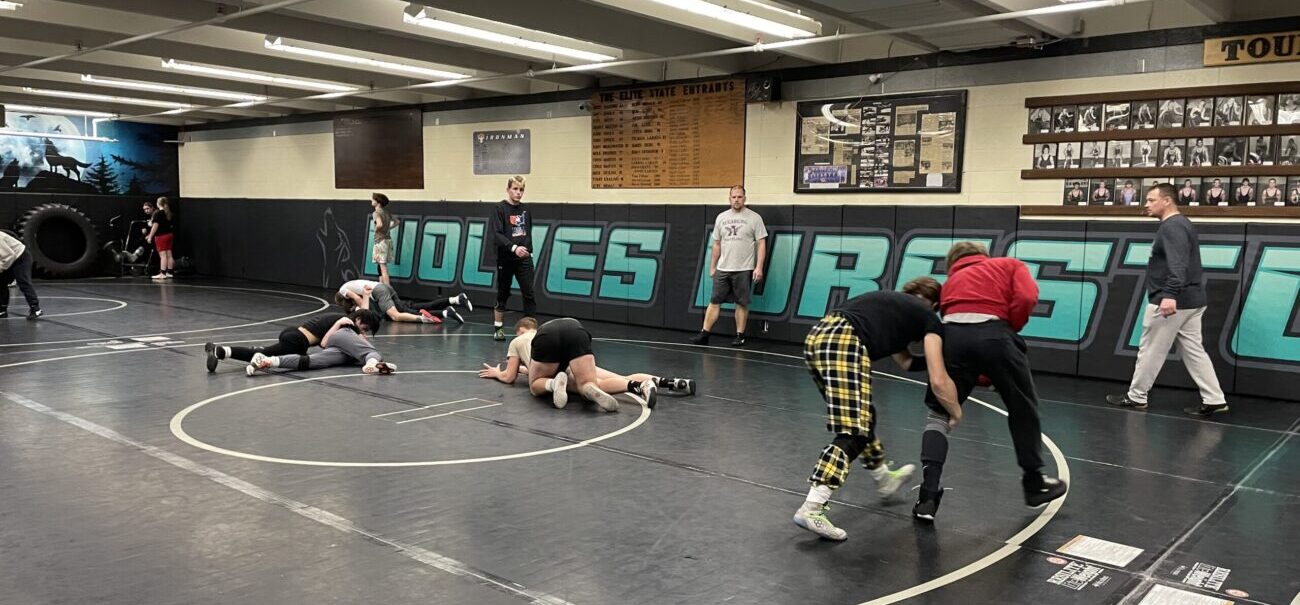 Wrestlers practice in a room that with black mats and Wolves Wrestling in bright green letters on the wall.