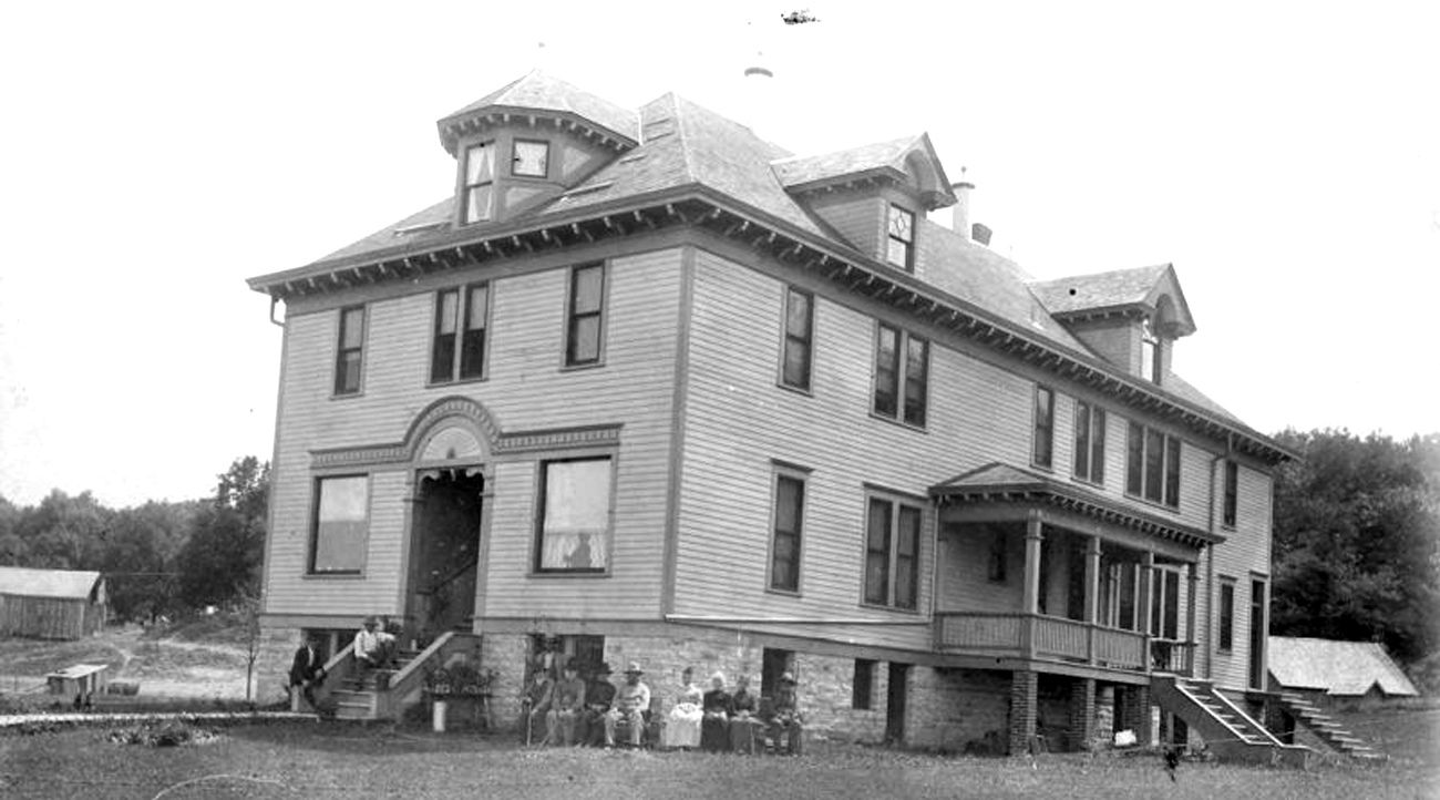 Black and white photo of an old two-story rectangular building with windows wrapping around the building.