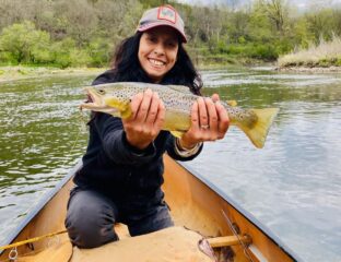 Women in a canoe holds a large brown trout with both hands.