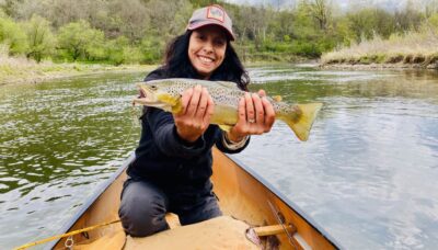 Women in a canoe holds a large brown trout with both hands.