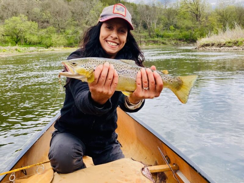 Women in a canoe holds a large brown trout with both hands.