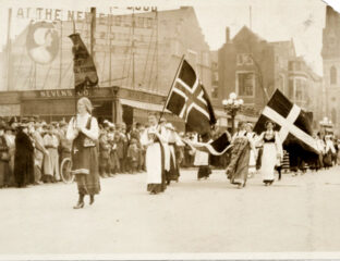 A black and white photo of women wearing long skirts marching in a parade under various Scandinavian flags.