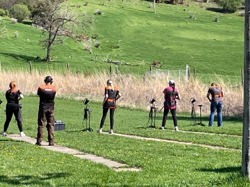 Students line up in a grassy area waiting to shoot at clay pigeons.