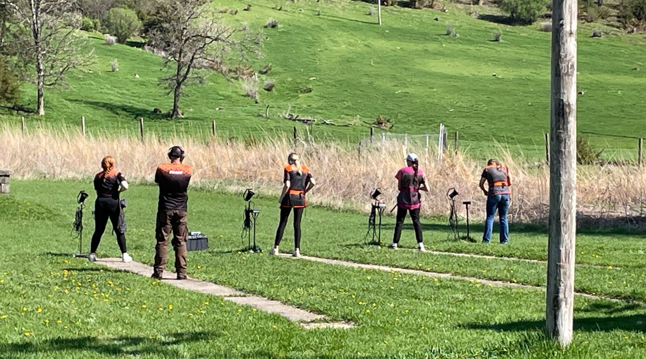 Students line up in a grassy area waiting to shoot at clay pigeons.