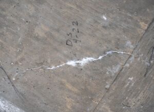 A crack in cement with white powdery filling with the initials DS 4-22 written next to it in black.