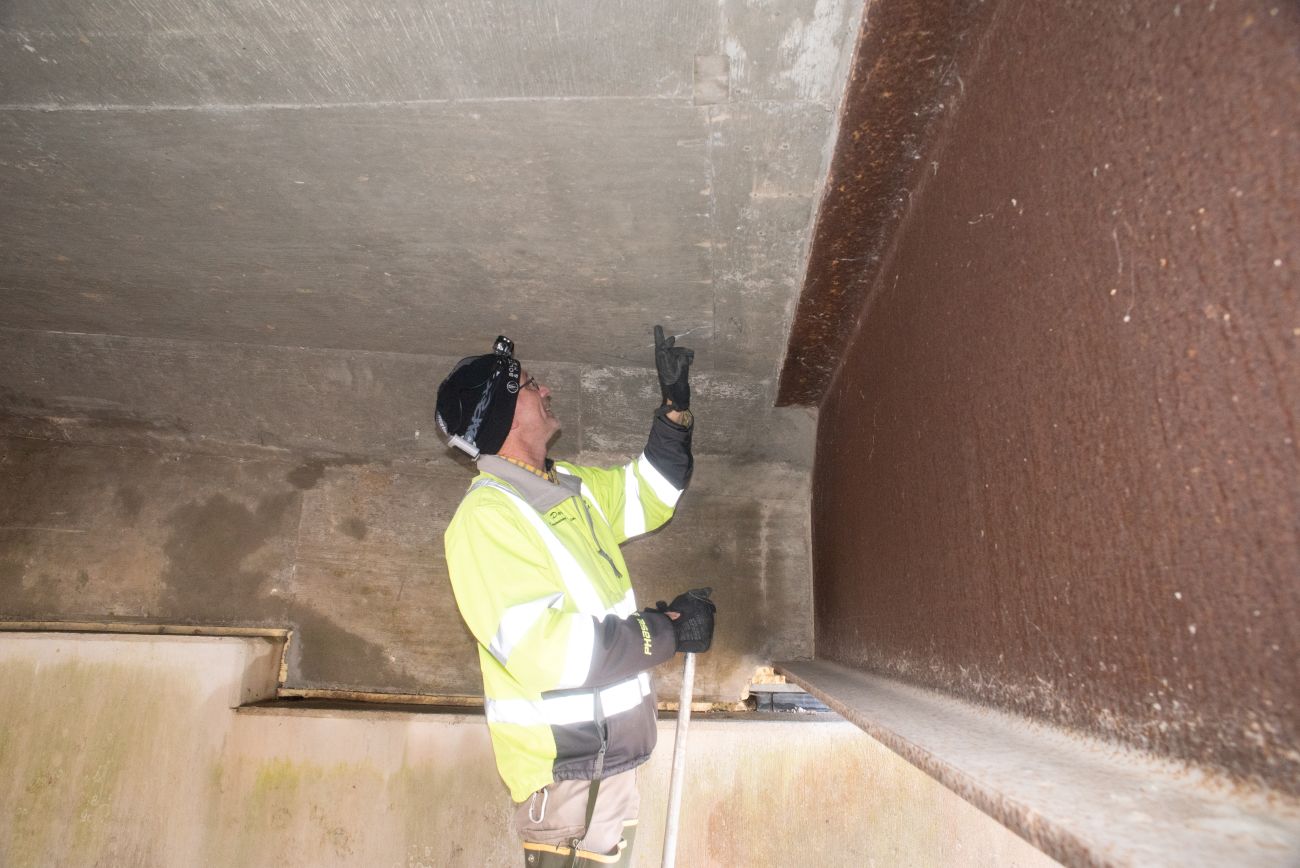 A man in a bright yellow vest stands under a cement and steel bridge.