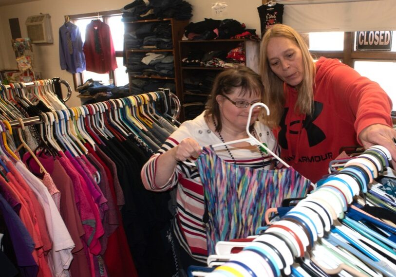 1 MIKKI AND KELLI Kelli Pierce, Activities Director at Thrifty Threads in Preston, helps Mikki hang donated clothing on the sale rack. (Photo by John Weiss)