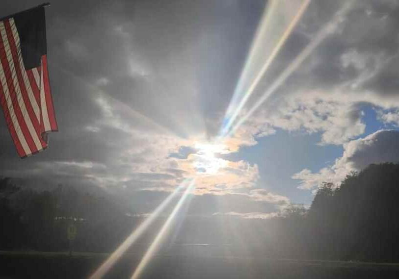 sunshine streams through the clouds with an American flag on the left