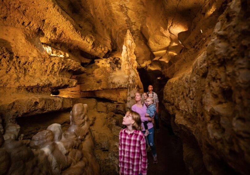 PHOTO 1 Cave of the Mounds family tours cave A family explores Cave of the Mounds, located in Dane County Wisconsin (link in article below). Cave of the Mounds takes its name from the Blue Mounds, two large hill landmarks. The main cavern began forming over a million years ago as water dissolved the limestone bedrock below the surface. (Photo courtesy of DARK Trail)