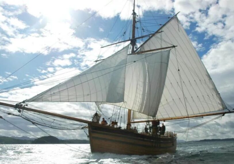 A replica of “The Restauration” Norwegian sailing ship shown at full sail on the sea with a bright blue sky with white clouds behind the sails.