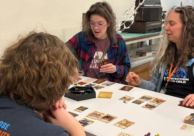 A group of four people sit around a small table with cards laid out in front of each person.