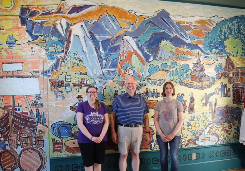PHOTO 1 Giants of the Earth Mural <span style="font-size: 14px; color: #6c6b6b; ">Giants of the Earth Heritage Center Staff in front of mural depicting Valdres, Norway, by late Norwegian artist Sigmund Aarseth. Left to right, Violet Hatfield, Bill Fried, Anastasia (Stacy) Wold. (Photo by Alison Leathers)</span>