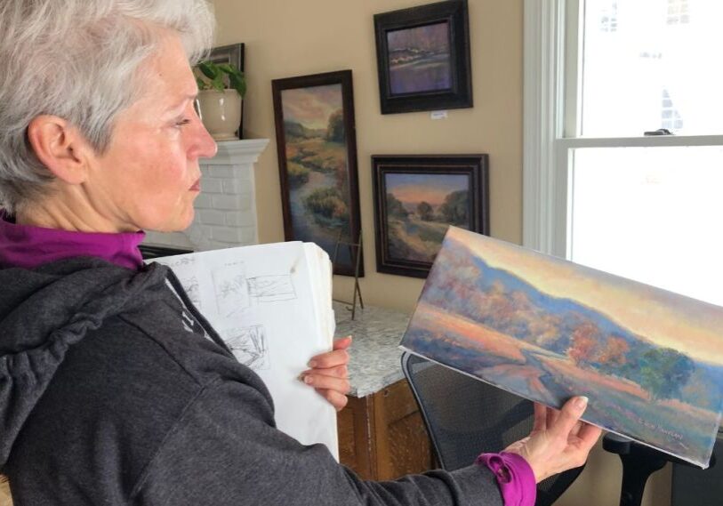 PHOTO 1 Joan Finnegan holds a painting A woman with short gray hair holds a small rectangular, unframed landscape painting in front of her.