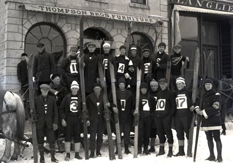 PHOTO 1 Ski jumpers in Lanesboro Black and white photo of a group of downhill skiers holding their skis upright in front of them with dark uniforms and large white labels on the front with their team numbers.