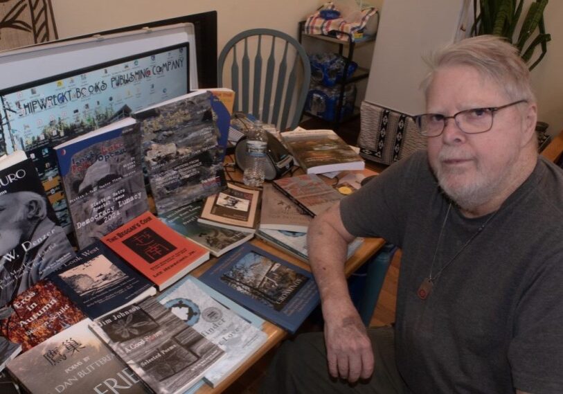 PHOTO 1 Tom Driscoll books he has published. man at table with book and magazine covers