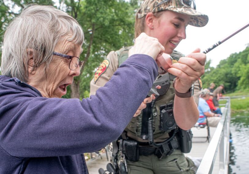 Photo 1 DNR QUAL If a picture can tell a thousand words, this is it! John Weiss captured the perfect picture to accompany his story about special needs fishing put on by the DNR. Pictured is Nancy Qual of Austin being assisted by Conservation Officer Annette Kyllo. (Photo by John Weiss)