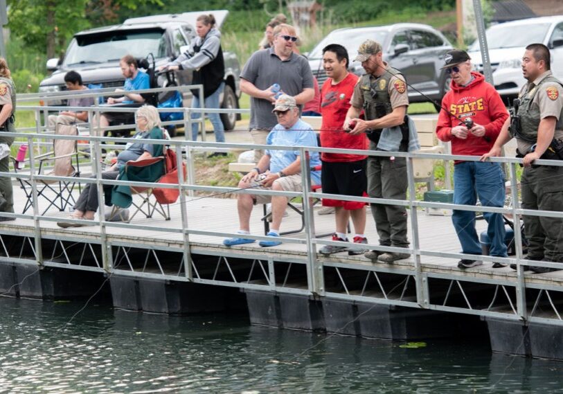 Photo 1 DNR SPECIAL People with special needs, state conservation officers and others, line the fishing pier at the pond in Sylvan Park in Lanesboro in June. (Photo by John Weiss)